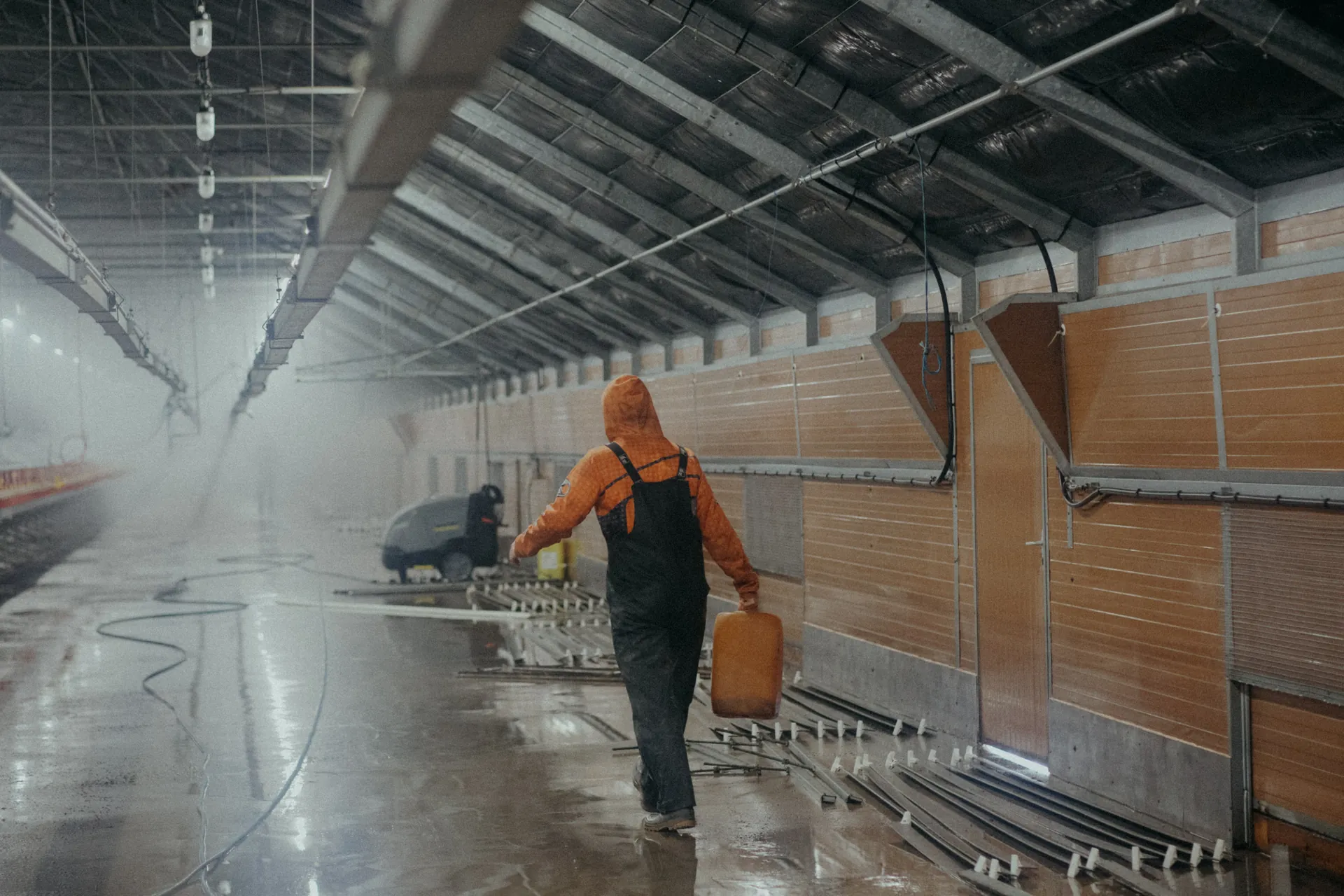 Un homme transporte un bidon dans un poulailler en tenue de travail. Photographié par Jeremy Dan, photographe d'entreprise basé à Sceaux.
