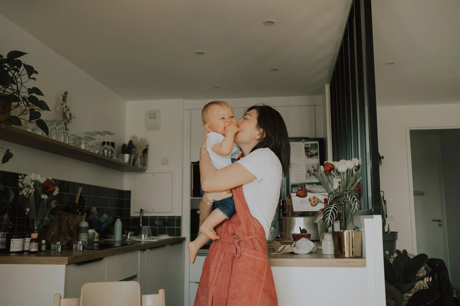 Une maman tient son enfant dans ses bras. Les deux sont heureux et rigolent ensemble. Photographié par Jeremy Dan, photographe de famille basé à Sceaux.