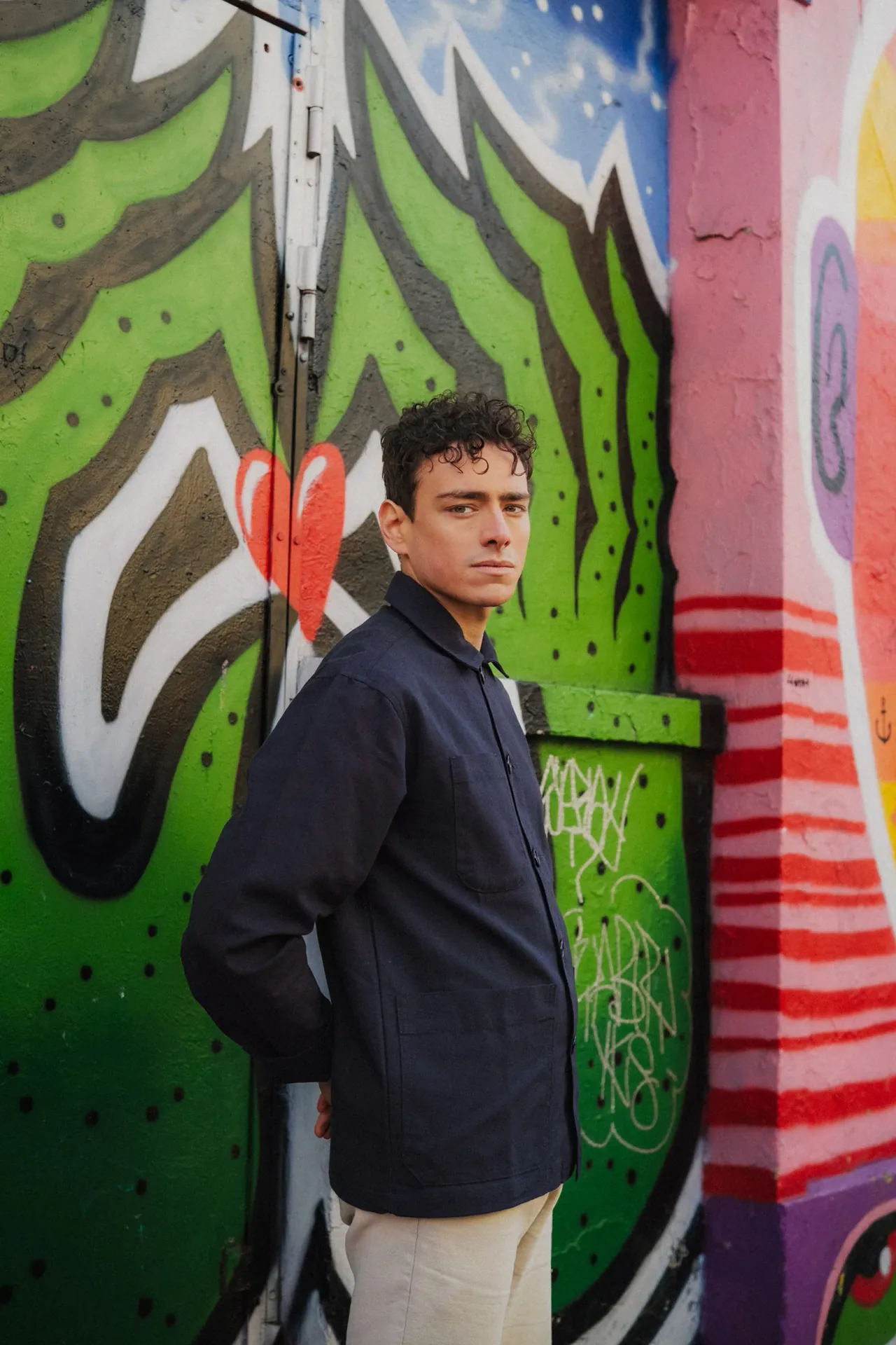 Un jeune homme modele met en avant sa surchemise en toile devant un mur décoré d'un grand graffiti.