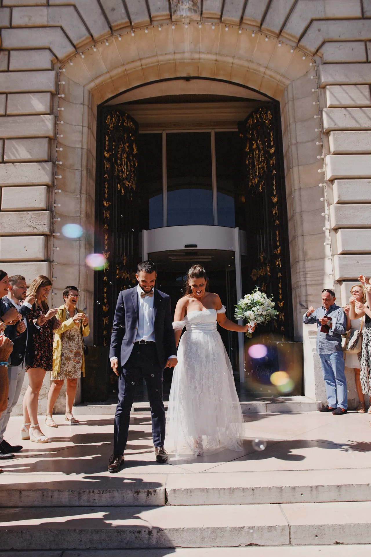 Le marié et la mariée sortent de la mairie en tenue de mariage acclamés par les invités.