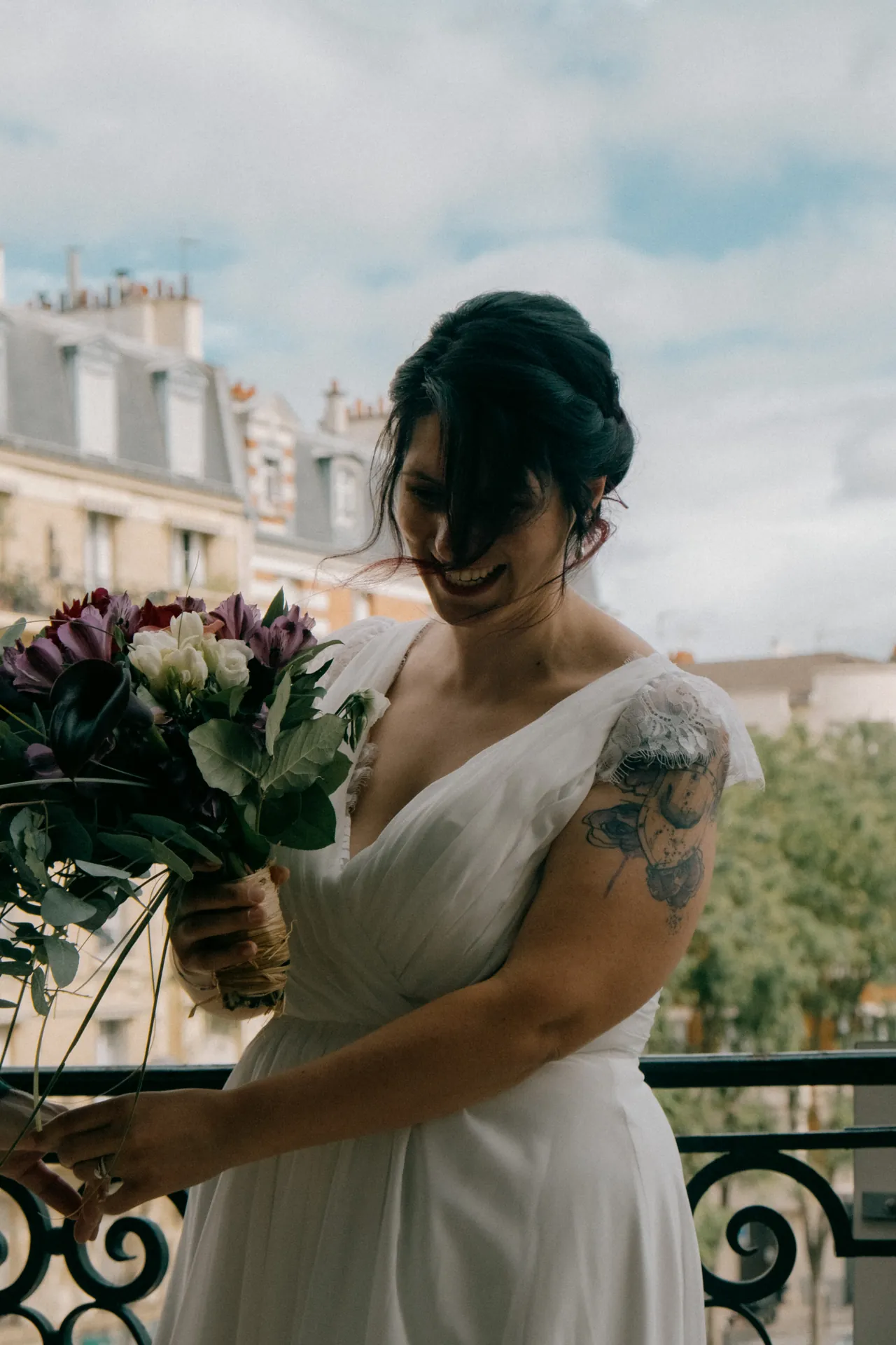 La mariée rigole avec un bouquet de fleurs sur le balcon de la mairie.
