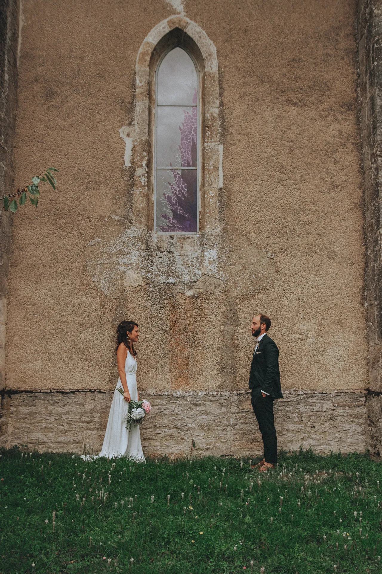Le marié et la mariée se regardent face à face devant l'église et sourient ensemble.