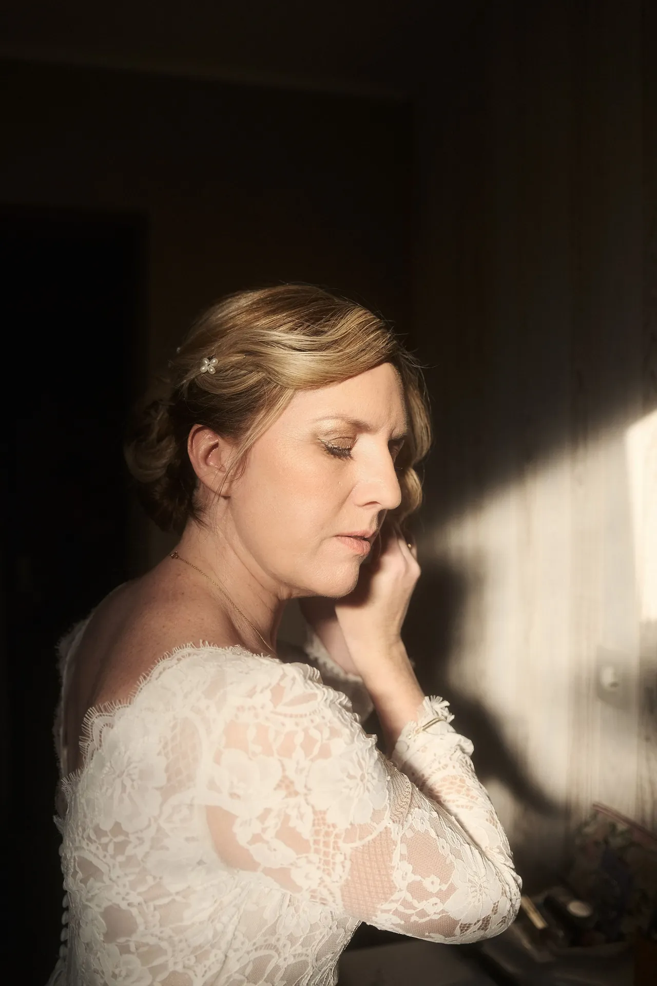 La mariée attache sa boucle d'oreille avec le soleil qui révèle une ambiance intimiste et chaleureuse.
