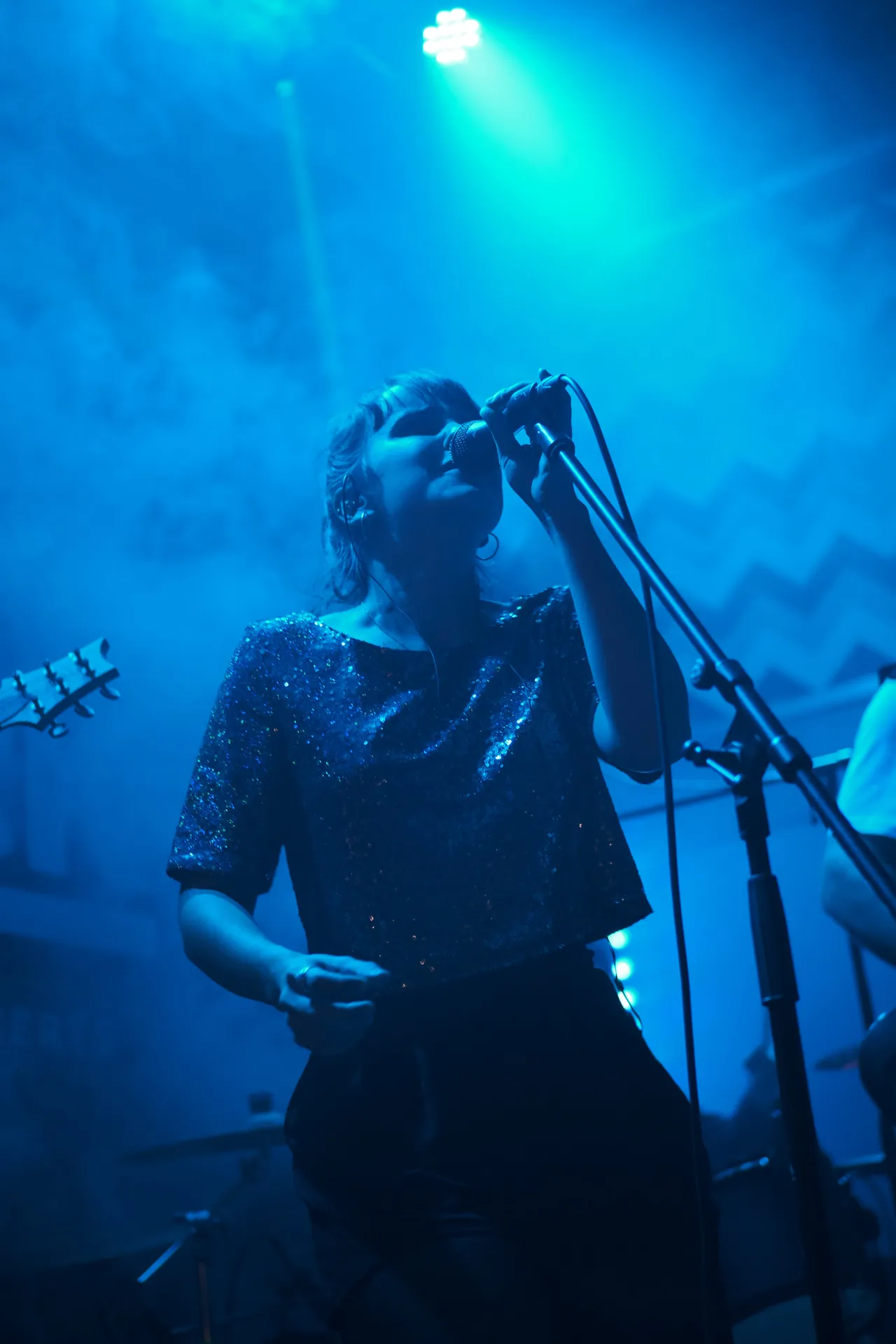 Une femme chante sur scène en concert avec son groupe de musique dans une ambiance de lumière bleue.