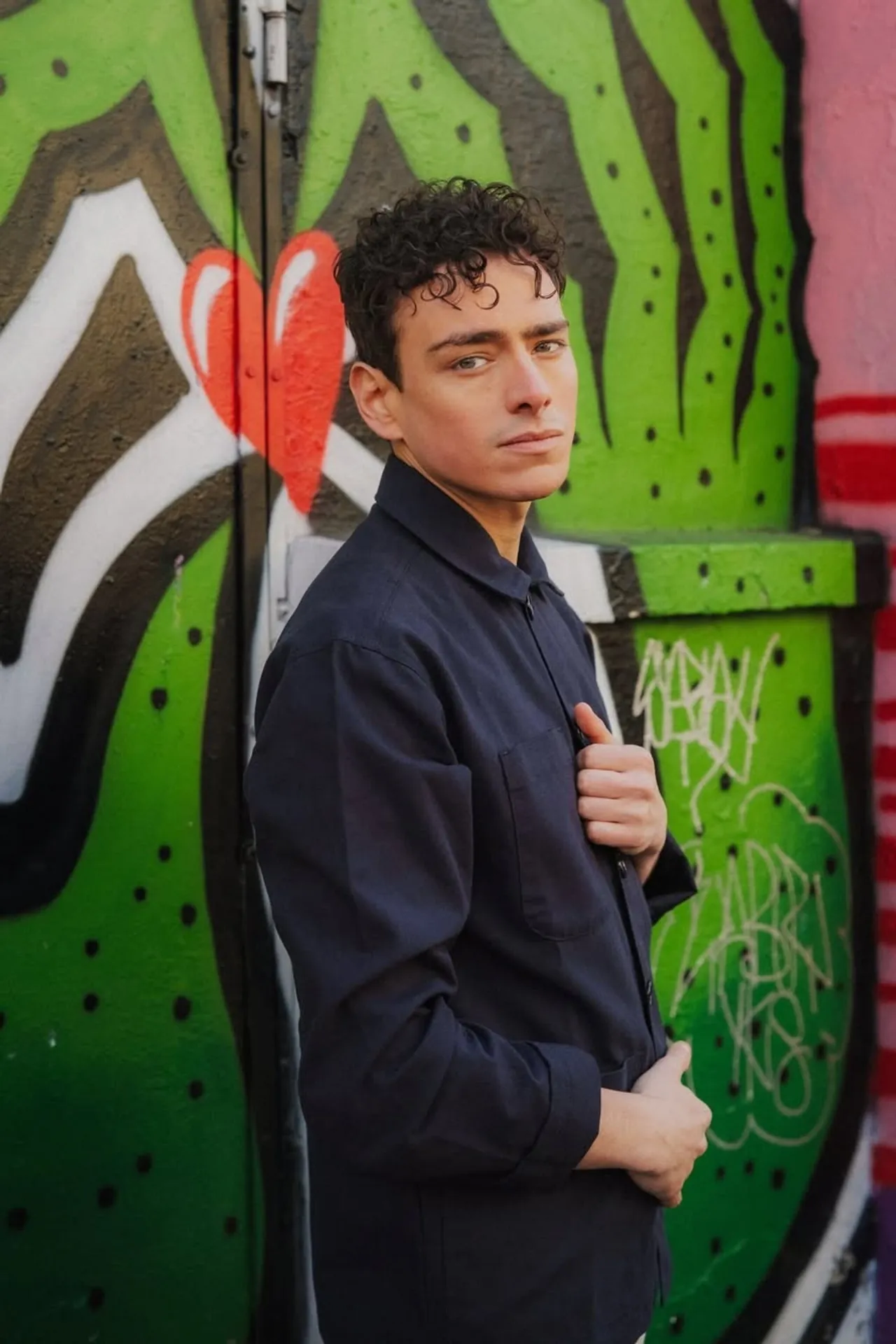 Un jeune homme mannequin met en avant sa surchemise devant un mur décoré par un grand graffiti lors d'un shooting professionnel réalisé par Jeremy Dan.