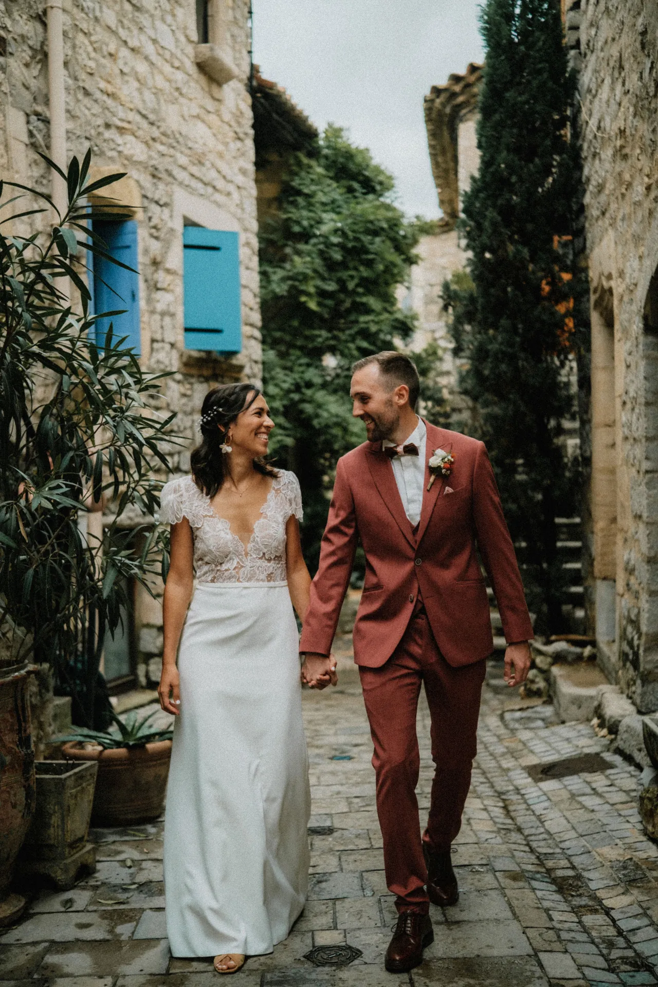 Le marié et la mariée marchent dans un petit village main dans la main en se regardant dans une ambiance bohême et chaleureuse.