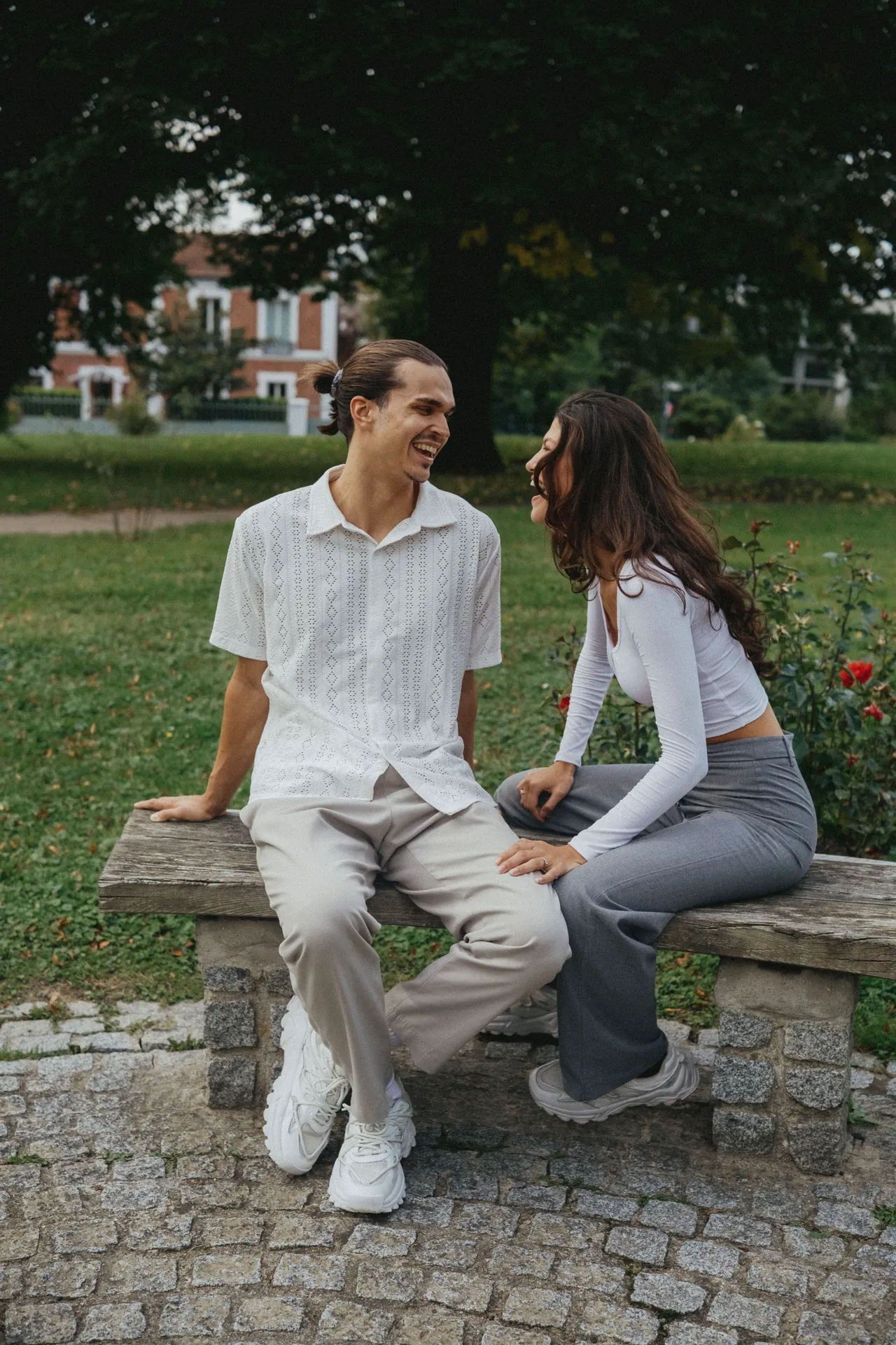 Un couple assis sur un banc se regarde et rigole ensemble dans un parc.