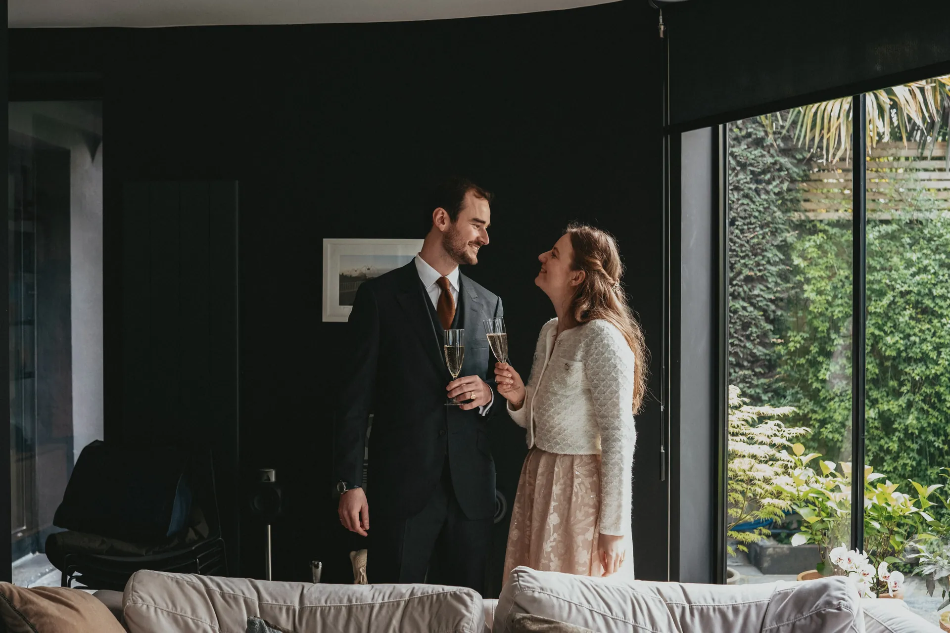 La marié et la mariée se regardent amoureusement et trinquent ensemble dans une belle maison avec une porte vitrée.