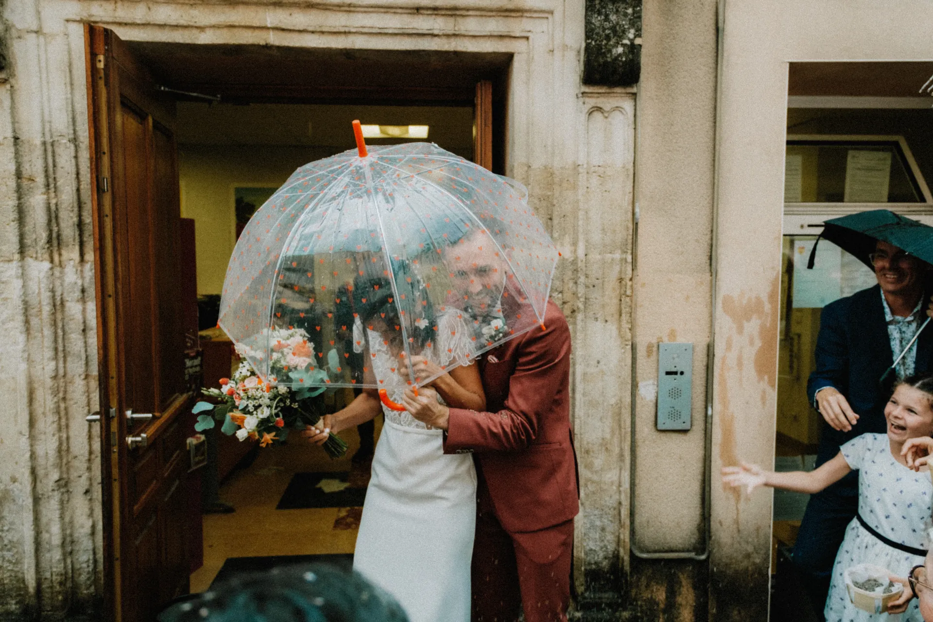 Deux mariés sortent de la mairie acclamés par les invités avec du riz. Les deux sont heureux et rigolent. Capturé par Jeremy Dan, photographe et vidéaste de mariage à Sceaux, Hauts-de-Seine.