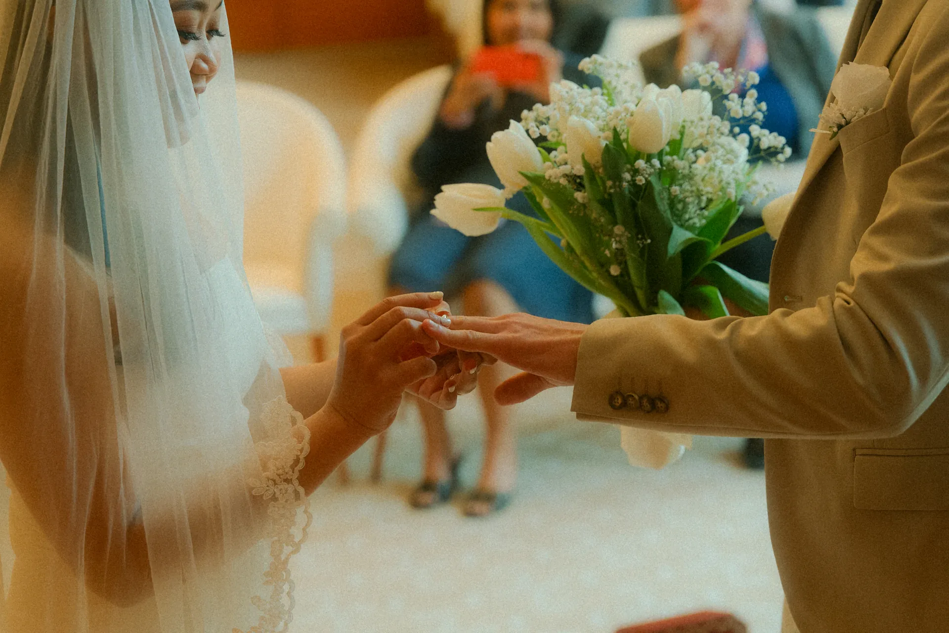 Le marié insère la bague de mariage dans le doigt de la mariée durant la célébration civile de leur mariage dans la mairie. Capturé par Jeremy Dan, photographe et vidéaste de mariage basé à Sceaux, Hauts-de-Seine.